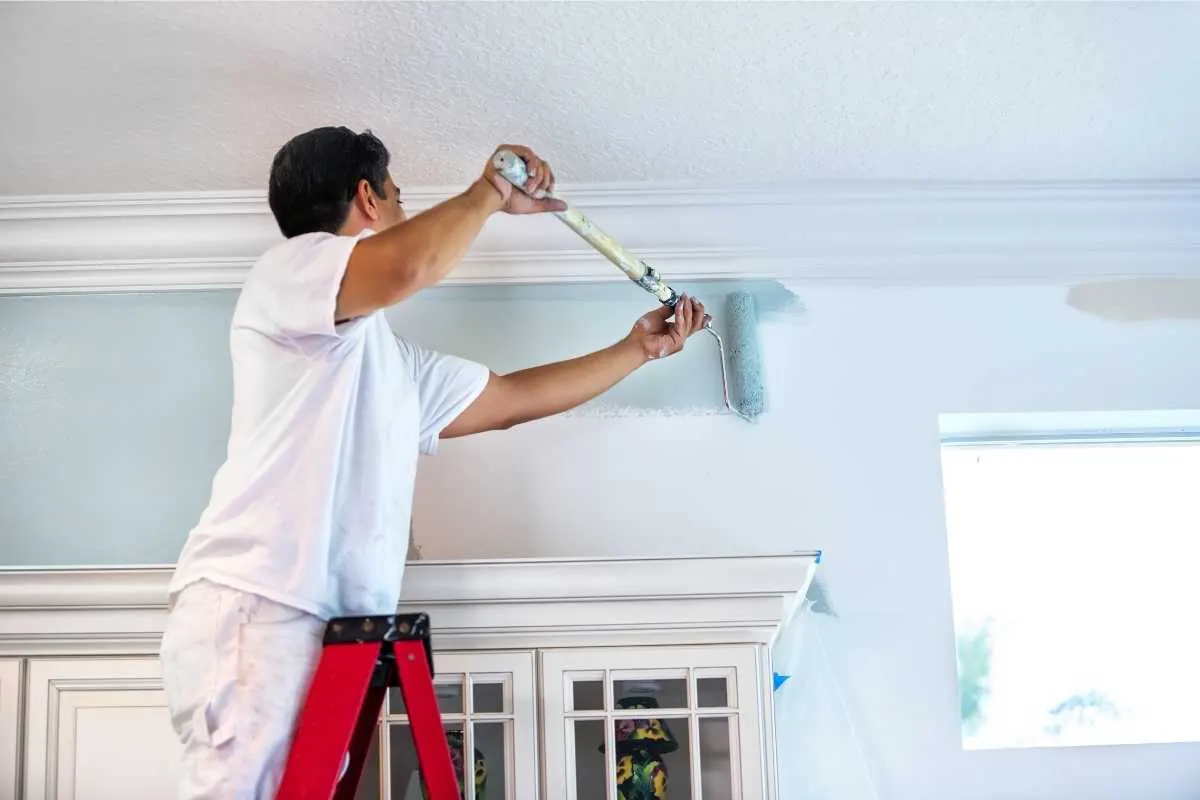 A painter cutting in along the ceiling line of an interior wall